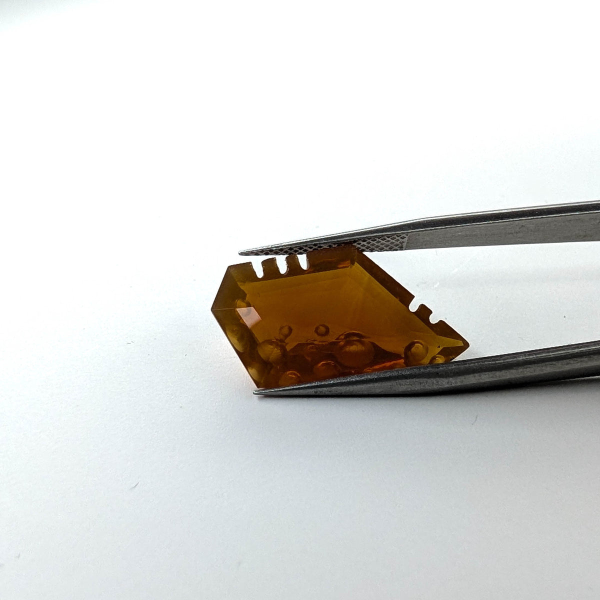 Oregon fire opal faceted freeform fantasy cut gemstone, 7.43ct, held in tweezers, view 2 of 13