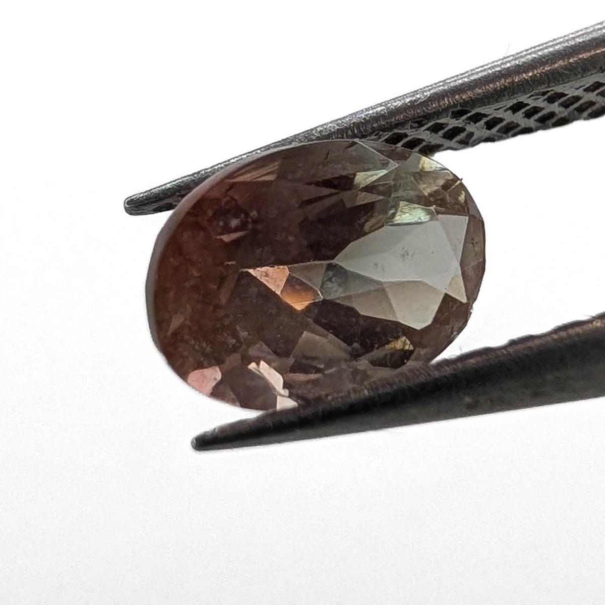 Oregon Sunstone faceted oval cut gemstone, 0.91ct, from Plush, Oregon, held in tweezers, view 2 of 11