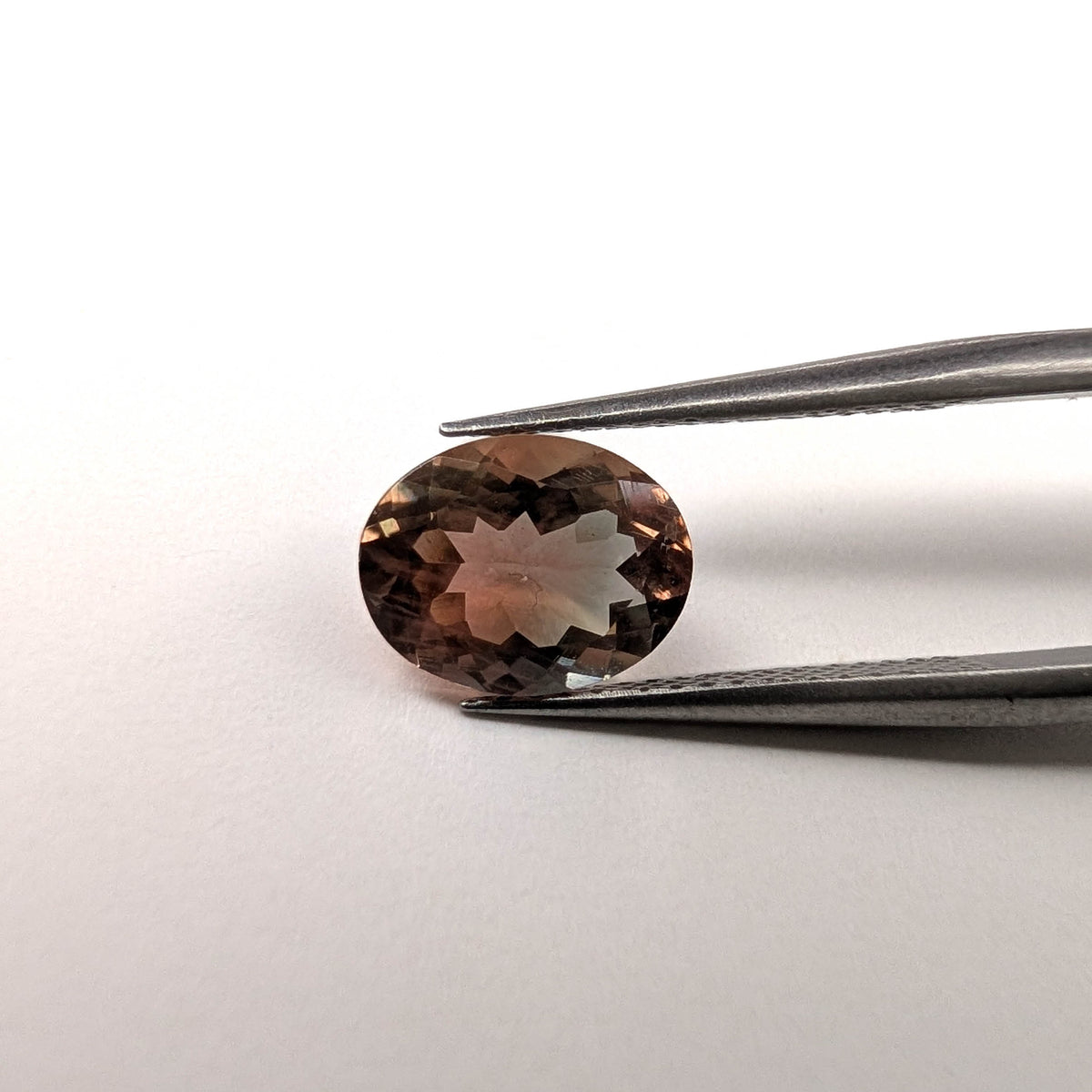 Oregon Sunstone faceted oval cut gemstone, 1.81ct, from Plush, Oregon, held in tweezers, view 2 of 11