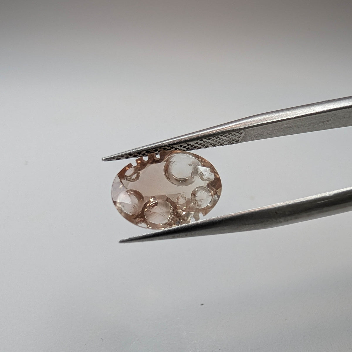 Oregon Sunstone faceted oval fantasy cut gemstone, 2.20ct, from Plush, Oregon, held in tweezers, view 2 of 11