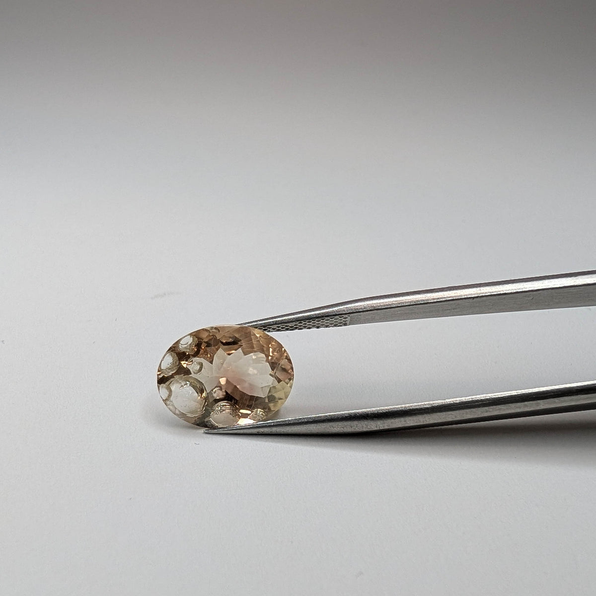 Oregon Sunstone faceted oval fantasy cut gemstone, 4.31ct, from Plush, Oregon, held in tweezers, view 3 of 10
