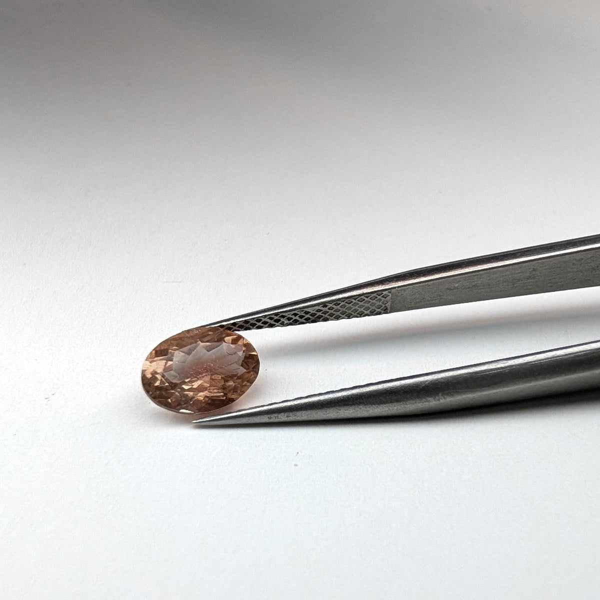 Oregon sunstone faceted oval gemstone, 1.18ct, held in tweezers