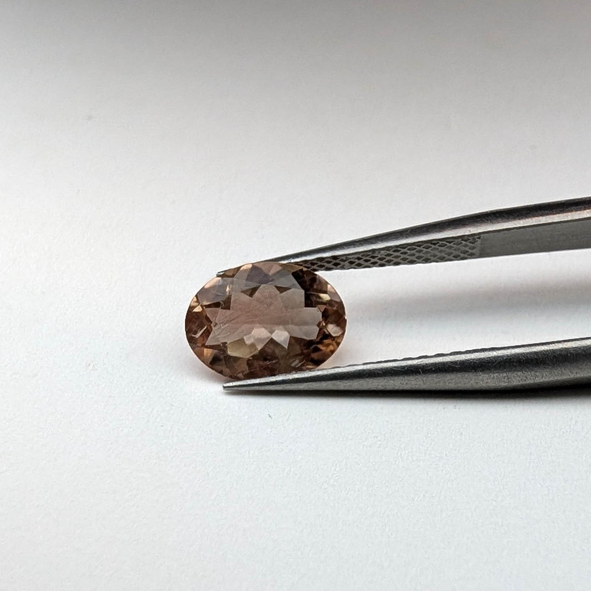 Oregon sunstone faceted oval gemstone, 1.36ct, held in tweezers