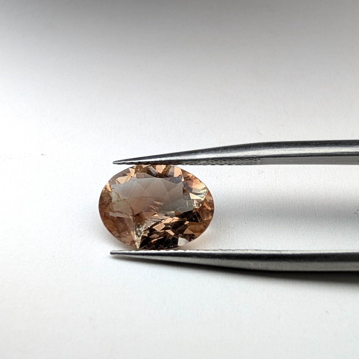 Oregon sunstone faceted oval gemstone, 3.06ct, held in tweezers