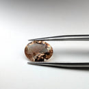 Oregon sunstone faceted oval gemstone, 3.06ct, held in tweezers