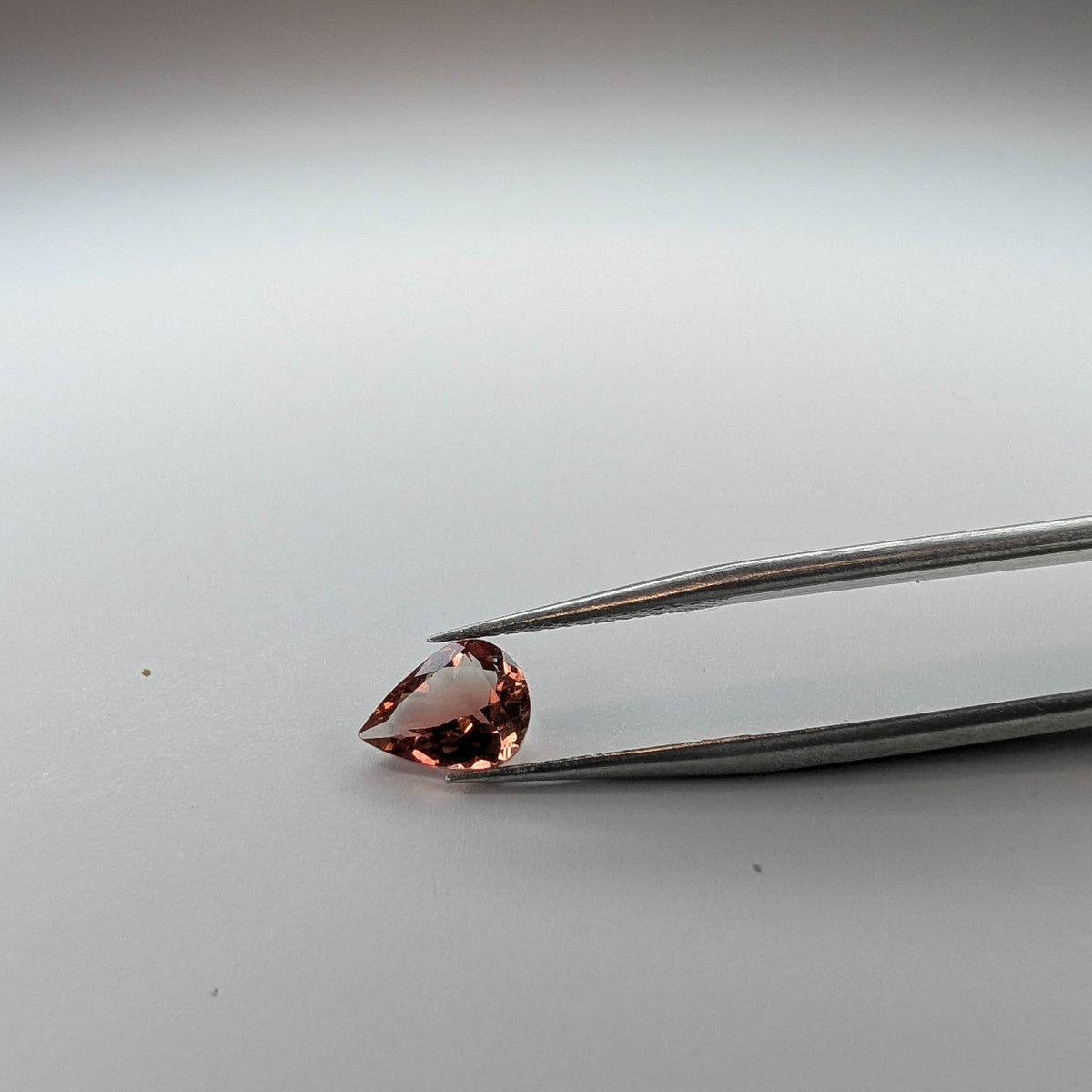 Oregon sunstone faceted pear gemstone, 1.32ct, held in tweezers
