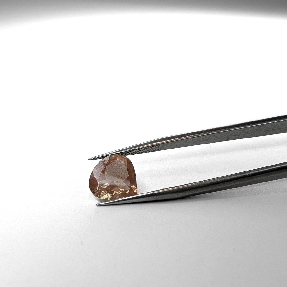 Oregon sunstone faceted pear gemstone, 2.72ct, held in tweezers