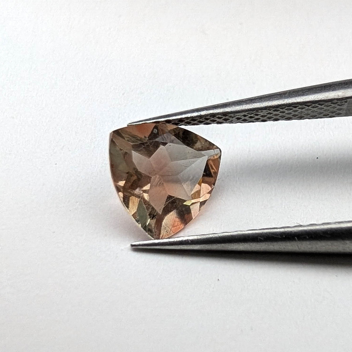 Oregon sunstone faceted trillion gemstone, 1.30ct, held in tweezers